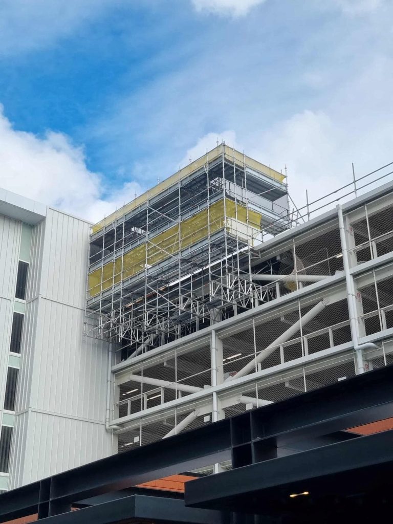 Scaffolding with yellow protective netting erected around the upper levels of a commercial building